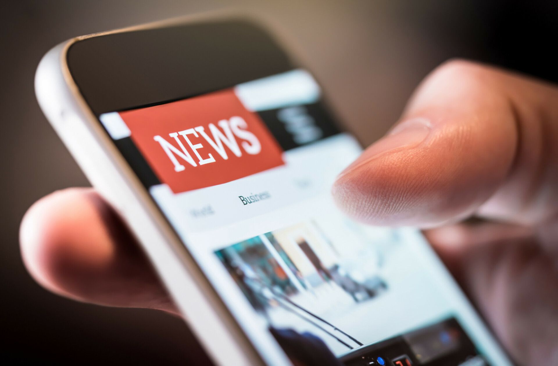 Nahaufnahme der Hand einer Person, die ein Smartphone benutzt und auf dem Bildschirm eine Nachrichten-Website mit einer prominenten „News“-Überschrift anzeigt.