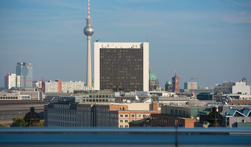 Skyline von Berlin mit dem Fernsehturm, einem großen, aus nachhaltigem Dämmstoff gebauten Hotel und anderen Gebäuden unter einem klaren blauen Himmel.