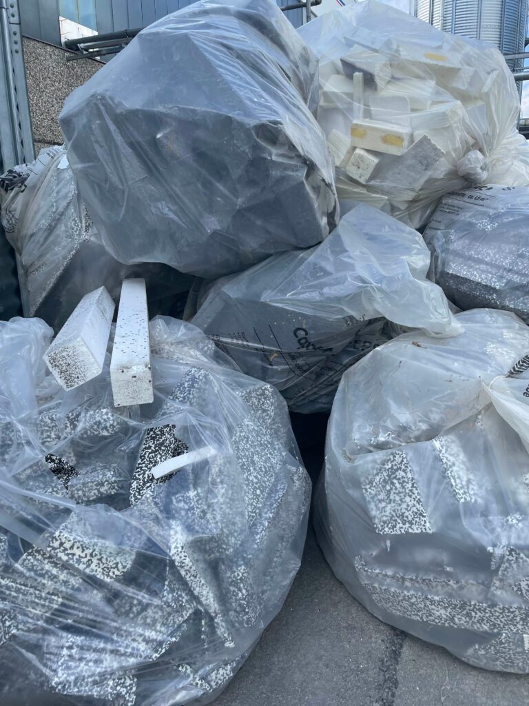 Mehrere große durchsichtige Plastiksäcke gefüllt mit verschiedenem Abfall, darunter Styroporstücke und schwarze und weiße Materialien, sammelten sich neben einem grauen Gebäude.